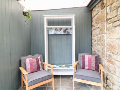 A small seating area with two cushioned chairs and a white coat rack against a stone and wood paneled wall at Polgear View Polgear Nr Redruth