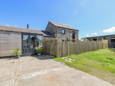 An outdoor view of a stone house with a wooden extension and black double doors next to a wooden fence and a grassy area at Polgear View in Polgear Nr Redruth