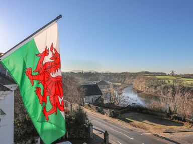 A Welsh flag flying beside a road with a river and trees in the background at Bryn Min Manton Apartment in Caernarfon