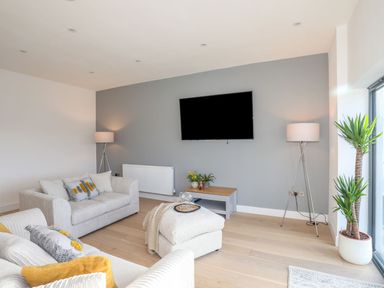 A living room with two sofas a TV on a wall and floor lamps at Bryn Min Manton Apartment in Caernarfon