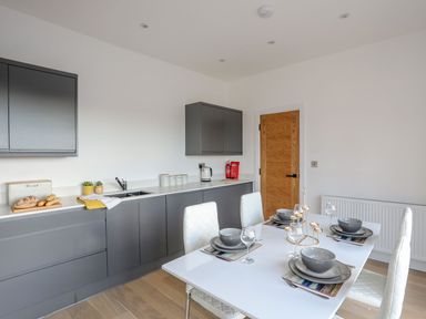 A kitchen with gray cabinets a white dining table set with dishes and white chairs at Bryn Min Manton Apartment in Caernarfon
