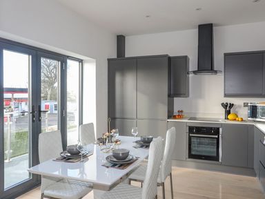 A kitchen with grey cabinets a dining table with four white chairs and place settings at Bryn Min Manton Apartment in Caernarfon