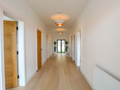 A hallway with wooden doors on both sides light fixtures on the ceiling and plants near glass doors at Bryn Min Manton Apartment in Caernarfon