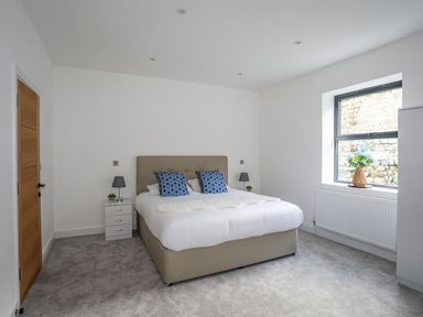 A bedroom with a bed with blue patterned pillows bedside tables with lamps and a window with flowers on the sill at Bryn Min Manton Apartment in Caernarfon