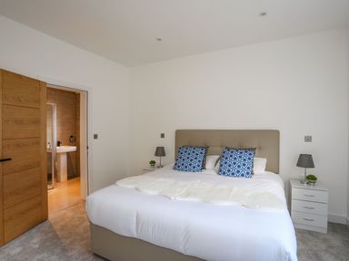 A bedroom with a bed with blue patterned pillows two bedside tables with lamps and plants an open door leading to a bathroom at Bryn Min Manton Apartment in Caernarfon