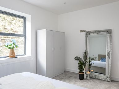 A bedroom with a white wardrobe next to a window and a large ornate mirror with plants and candles at Bryn Min Manton Apartment in Caernarfon