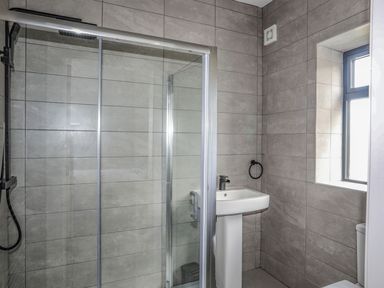 A bathroom with a tiled shower enclosure a pedestal sink a window and a toilet at Bryn Min Manton Apartment Caernarfon