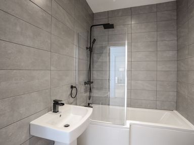 A bathroom with a white sink black faucet and a bathtub with a glass shower screen at Bryn Min Manton Apartment in Caernarfon