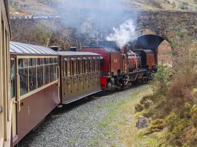 A steam train passing under a stone arch bridge on a rural railway track