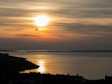 A sunset over water with a silhouette of land and buildings at Bryn Min Manton Apartment in Caernarfon