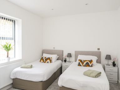 A bedroom with two single beds nightstands and a window with a plant at Bryn Min Manton Apartment in Caernarfon