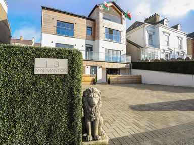 A modern residential building with balconies and a driveway with a lion statue at Bryn Min Manton Bach in Caernarfon