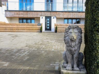 A lion statue on a paved driveway in front of a modern house with a black door at Bryn Min Manton Bach in Caernarfon