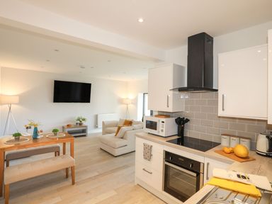 A kitchen and living area with an oven, microwave, dining table, sofa and wall mounted tv at Bryn Min Manton Bach in Caernarfon