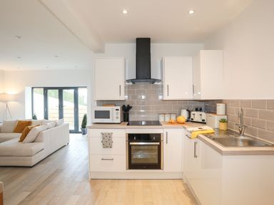 A kitchen with white cabinets oven microwave and sink next to a living area with sofa at Bryn Min Manton Bach in Caernarfon