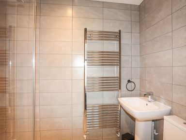 A bathroom with tiled walls a white sink a toilet and a chrome towel radiator at Bryn Min Manton Bach in Caernarfon