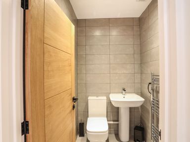 A small bathroom with a toilet sink wooden door and tiled walls at Bryn Min Manton Bach in Caernarfon