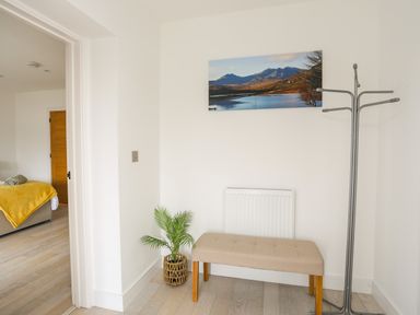 A hallway with a beige bench plant and coat rack at Bryn Min Manton Bach in Caernarfon