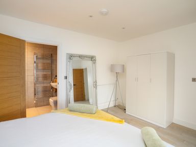 A bedroom with a white wardrobe a floor lamp a large decorative mirror and a view into a bathroom at Bryn Min Manton Bach in Caernarfon