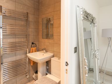 A bathroom with a pedestal sink toilet heated towel rack and a mirror next to a room with a standing mirror and a floor lamp at Bryn Min Manton Bach in Caernarfon