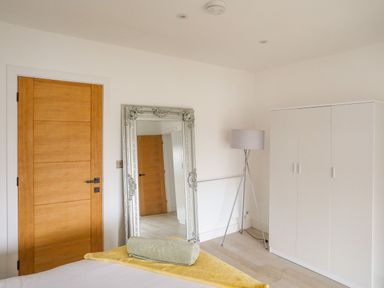 A bedroom with a wooden door a large decorative mirror a floor lamp a white wardrobe and a bed with folded towels at Bryn Min Manton Bach in Caernarfon