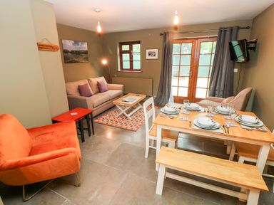 A living room with sofas a dining table set with plates and glasses and wooden benches at Bwthyn Canol in Haverfordwest