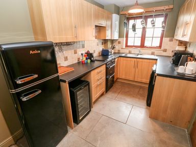 A kitchen with wooden cabinets black appliances tiled backsplash and floor at Bwthyn Canol in Haverfordwest