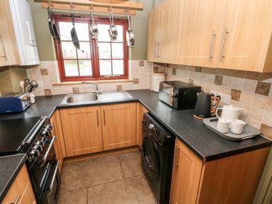 A kitchen with wooden cabinets black countertops a stove toaster kettle sink and washing machine at Bwthyn Canol in Haverfordwest