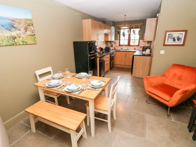 A kitchen and dining area with a wooden dining table set for four a black fridge wooden cabinets and an orange armchair at Bwthyn Canol in Haverfordwest