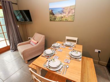 A dining area with a wooden table set for four people a beige armchair and a wall-mounted television at Bwthyn Canol in Haverfordwest