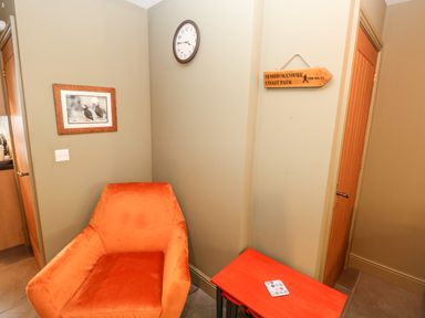 An orange armchair next to a red table with a coaster on it a clock on the wall a framed picture of birds and a wooden sign reading Pembrokeshire Coast Path at Bwthyn Canol in Haverfordwest