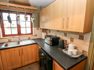 A kitchen with wooden cabinets a black countertop a sink a washing machine and hanging pots at Bwthyn Canol in Haverfordwest