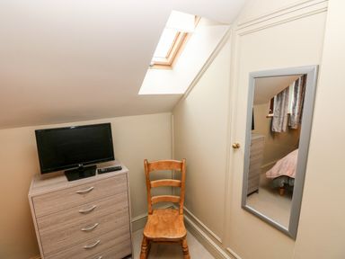 A room corner with a wooden chair next to a chest of drawers with a TV on top and a wall mirror reflecting part of the room at Bwthyn Canol in Haverfordwest