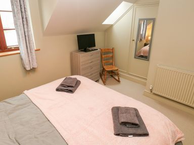 A bedroom with a bed, wooden chair, chest of drawers with a TV, window with curtains, and a wall mirror at Bwthyn Canol in Haverfordwest