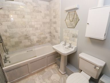 A bathroom with a bathtub and shower, a pedestal sink with dual taps, a toilet, and a wall-mounted cabinet at Bwthyn Canol in Haverfordwest