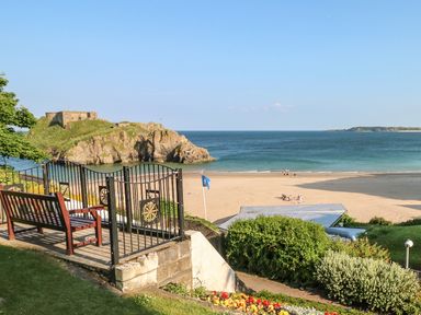 A bench and metal gate overlooking a sandy beach with people near the water and rocky island in the sea at Bwthyn Canol in Haverfordwest