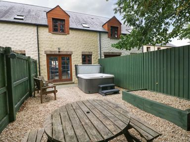 A backyard with a wooden table and chairs a hot tub and green fences at Bwthyn Canol in Haverfordwest
