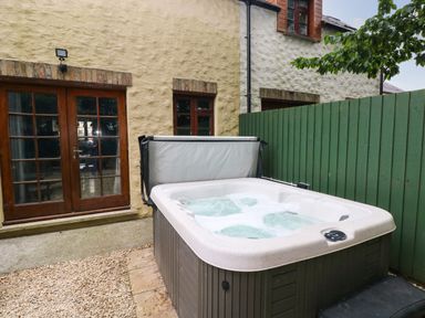 An outdoor patio area with a hot tub near a green wooden fence and stone walls at Bwthyn Canol in Haverfordwest