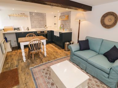A kitchen and living area with a wooden dining table two chairs a blue sofa a white coffee table and a floor lamp at Gelli Bach at Gelli Las in Llanbedr