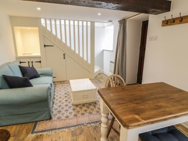 A living room with a blue sofa a wooden table and a white chest under stairs at Gelli Bach at Gelli Las in Llanbedr