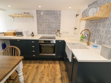 A kitchen with wooden floor blue cabinets oven sink and shelves with dishes at Gelli Bach at Gelli Las in Llanbedr