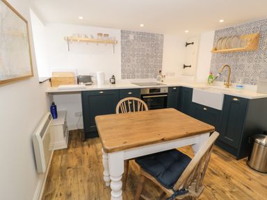 A kitchen with wooden dining table and chairs blue cabinets tiled backsplash and white countertop at Gelli Bach at Gelli Las in Llanbedr