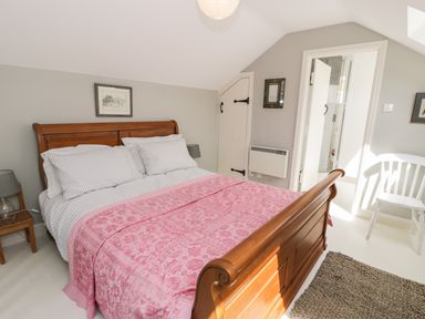 A bedroom with a wooden bed with pink patterned bedding a wooden nightstand lamp a white chair and a rug at Gelli Bach at Gelli Las in Llanbedr