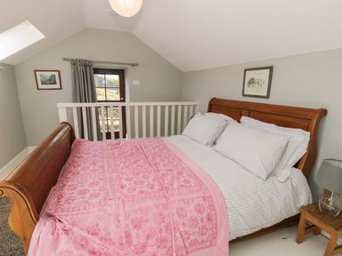 A bedroom with a wooden sleigh bed with white striped bedding and a pink patterned blanket at Gelli Bach at Gelli Las in Llanbedr