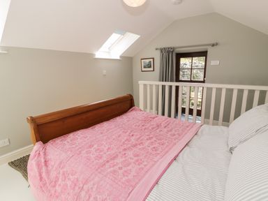 A bedroom with a wooden bed with pink cover near a window and skylight at Gelli Bach at Gelli Las in Llanbedr