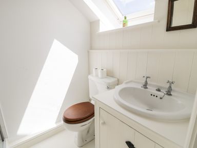 A bathroom with a toilet with a wooden seat and a sink under a skylight at Gelli Bach at Gelli Las in Llanbedr