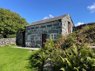 A stone cottage with a slate roof surrounded by grass and plants at Gelli Bach at Gelli Las in Llanbedr
