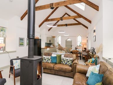 An open-plan living and dining area with leather sofas a wood-burning stove wooden ceiling beams and a kitchen at Ysgoldy Brynwyre in Llanrhystud
