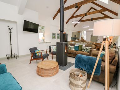 A living room with brown sofas blue chairs a wood stove and wooden ceiling beams at Ysgoldy Brynwyre in Llanrhystud