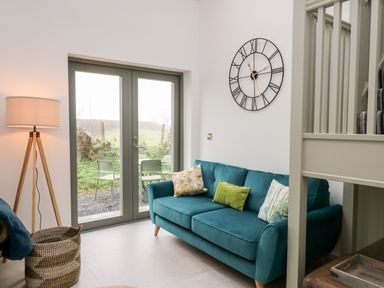 A living room with teal sofa and pillows next to glass doors with outdoor chairs visible at Ysgoldy Brynwyre in Llanrhystud